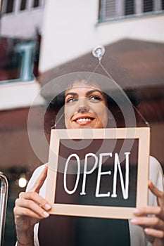 Smiling business woman putting an open sign on the glass door