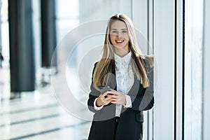 Smiling business woman standing in office with mobile phone in hand looking at camera