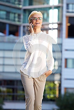 Smiling business woman walking outside with mobile phone