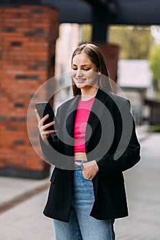 Smiling business woman walks down the central city street and uses her phone