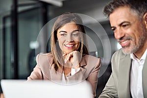 Smiling business woman working on laptop with male colleague at office meeting.