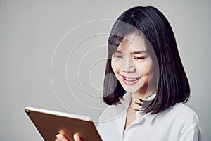 Smiling business women are holding tablet and using online applications. Gray background provides soft lighting.