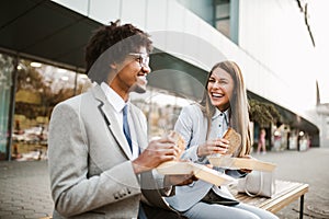 Businessman and businesswoman with sandwiches sitting in front of the office building - lunch break