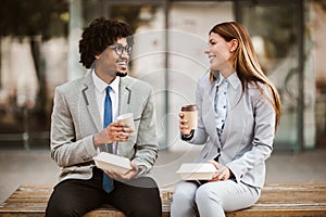 Businessman and businesswoman with sandwiches sitting in front of the office building - lunch break