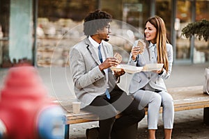 Businessman and businesswoman with sandwiches sitting in front of the office building - lunch break