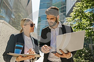 Smiling businessman and businesswomen working outdoor on laptop with new startup project