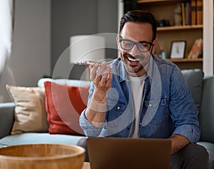 Smiling businessman checking e-mails over laptop and talking over smart phone in home office. Male freelancer using wireless