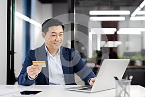 Smiling businessman with credit card making online payment