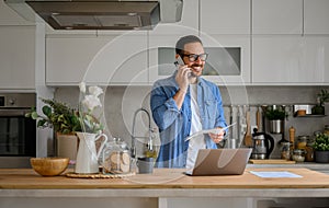Smiling businessman discussing over smart phone while working over laptop at kitchen counter at home
