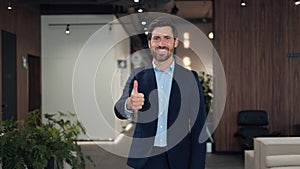 Smiling businessman doing positive gesture with thumb up at modern workplace