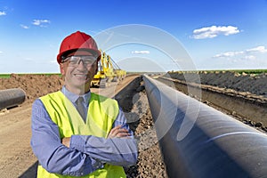 Smiling Businessman or Engineer in Red Hardhat Standing Next to Oil or Gas Pipeline