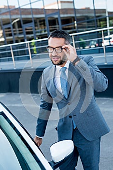 smiling businessman in eyeglasses opening car door