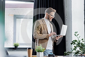 Smiling businessman in eyeglasses using laptop