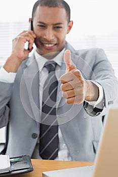 Smiling businessman gesturing thumbs up while on call