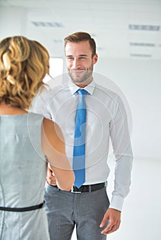 Smiling businessman greeting businesswoman with handshake in new office