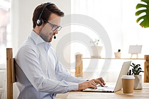 Smiling businessman in headset working on laptop make conference videocall