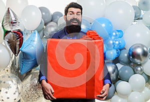 Smiling businessman with helium balloons with big present. Birthday celebration. Happy Bearded man with gift box.