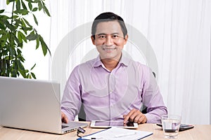 Smiling businessman at his desk with laptop and documents in his