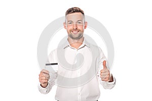 Smiling businessman holding credit card and showing thumb up isolated on white