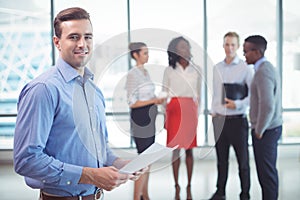 Smiling businessman holding documets with colleagues standing in background