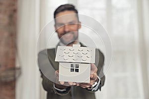 smiling businessman holding symbolic architectural house model focus on foreground