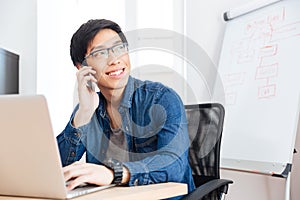 Smiling businessman with laptop talking on mobile phone in office