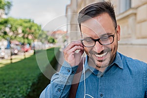 Smiling businessman listening music through headphones on sidewalk at the city