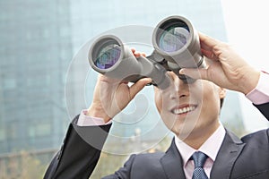 Smiling businessman looking through binoculars, blue reflection in the glass