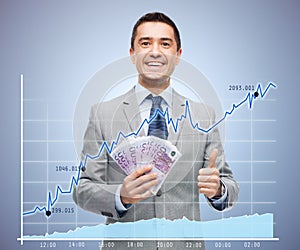 Smiling businessman with money showing thumbs up