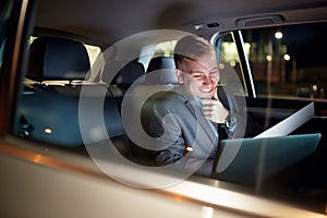 Smiling businessman in moving car working on his laptop