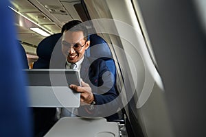 Smiling businessman passenger checking news digital tablet, using wireless connection on board during flight