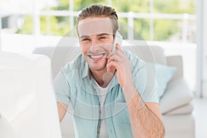 Smiling businessman on the phone while using computer
