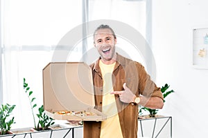 Smiling businessman pointing with finger at box with pizza in office