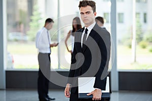 Smiling Businessman posing while colleagues talking together in office.