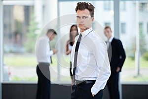 Smiling Businessman posing while colleagues talking together in office.