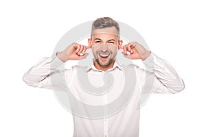 Smiling businessman putting fingers in ears isolated on white