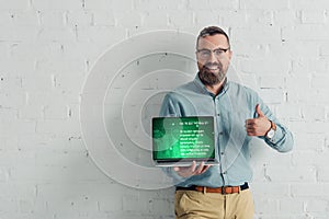 Smiling businessman showing thumb up and holding laptop with health website