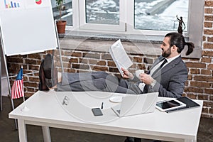 smiling businessman sitting at table, putting feet up and reading contract