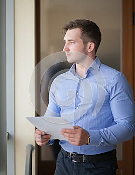 Smiling businessman standing by the window in office and reading