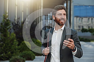 Smiling Businessman in suit going home after long working day and using phone