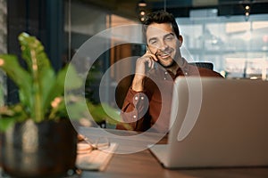 Smiling businessman talking on a cellphone while working late