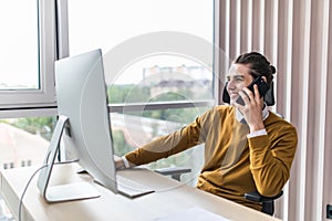 Smiling businessman talking on mobile phone while working on computer. Man sitting at his work table working on computer at home