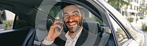 Smiling businessman talking phone with client while sitting on car backseats