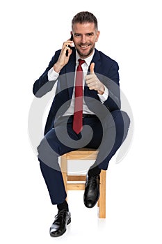 Smiling businessman talking on the phone and making thumbs up gesture