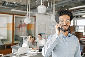 Smiling businessman talking phone standing in office on colleagues background