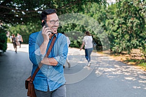 Smiling businessman talking on smart phone while walking on road against plants