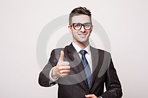 Smiling businessman with thumb up on gray background