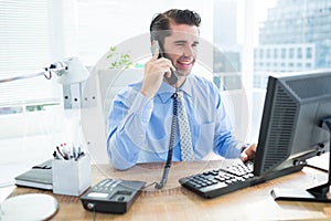 Smiling businessman using his computer ans phoning