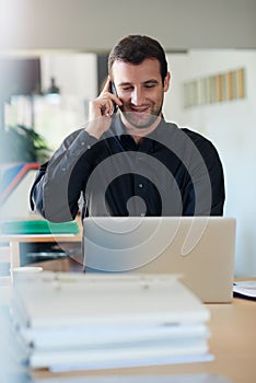 Smiling businessman using a laptop and talking on the phone