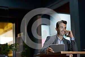 Smiling businessman using a tablet and talking on his cellphone